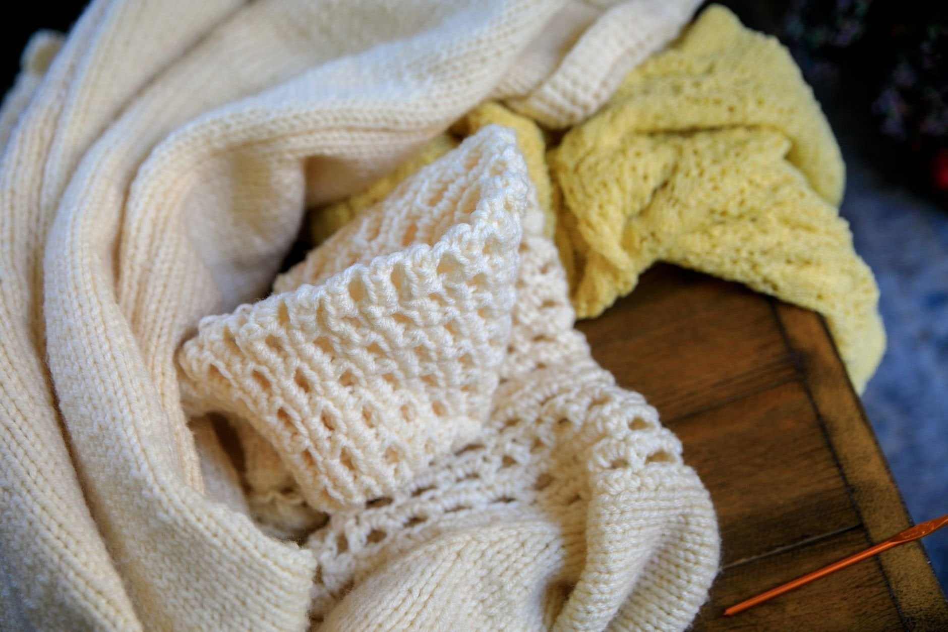 Soft wool knit sweaters in neutral tones arranged on a rustic wooden table